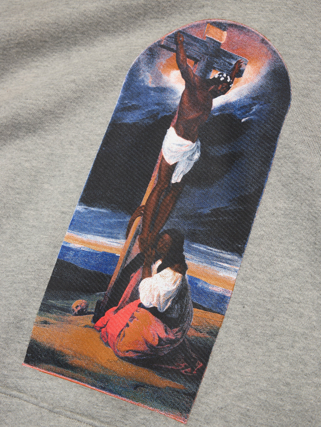 Gray Denim Tears hoodie with a graphic of a person on a cross and another person kneeling, set against a dark background.
